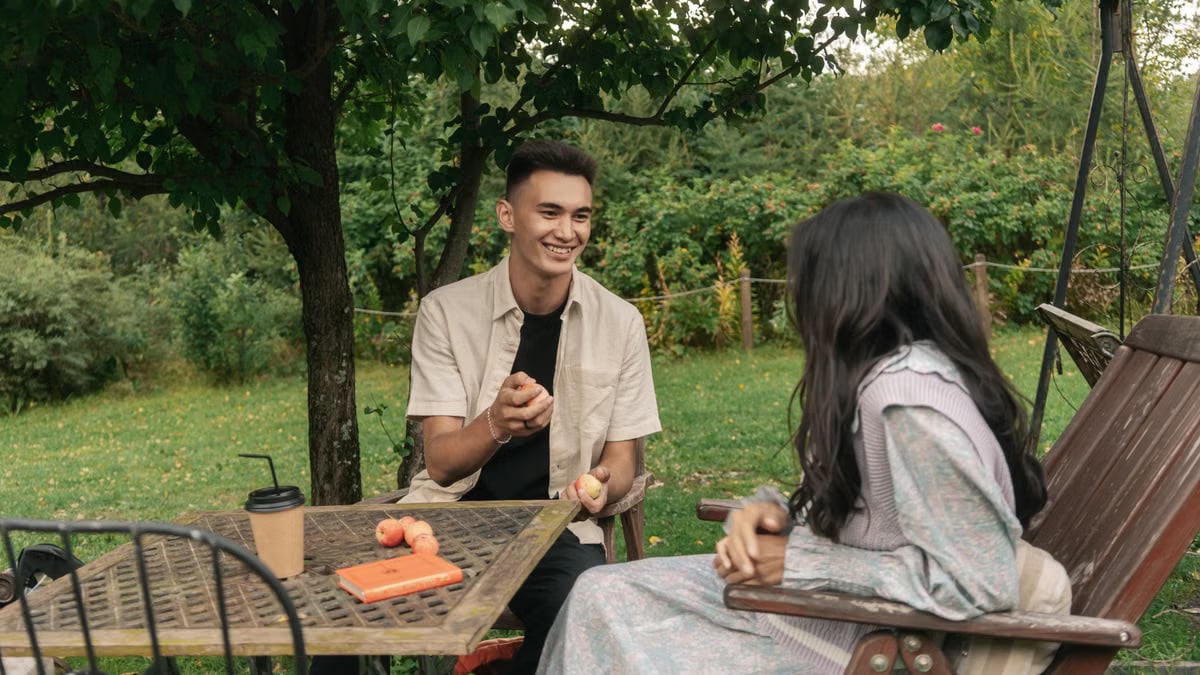 A couple enjoying a casual conversation with coffee and apples in a tranquil garden.